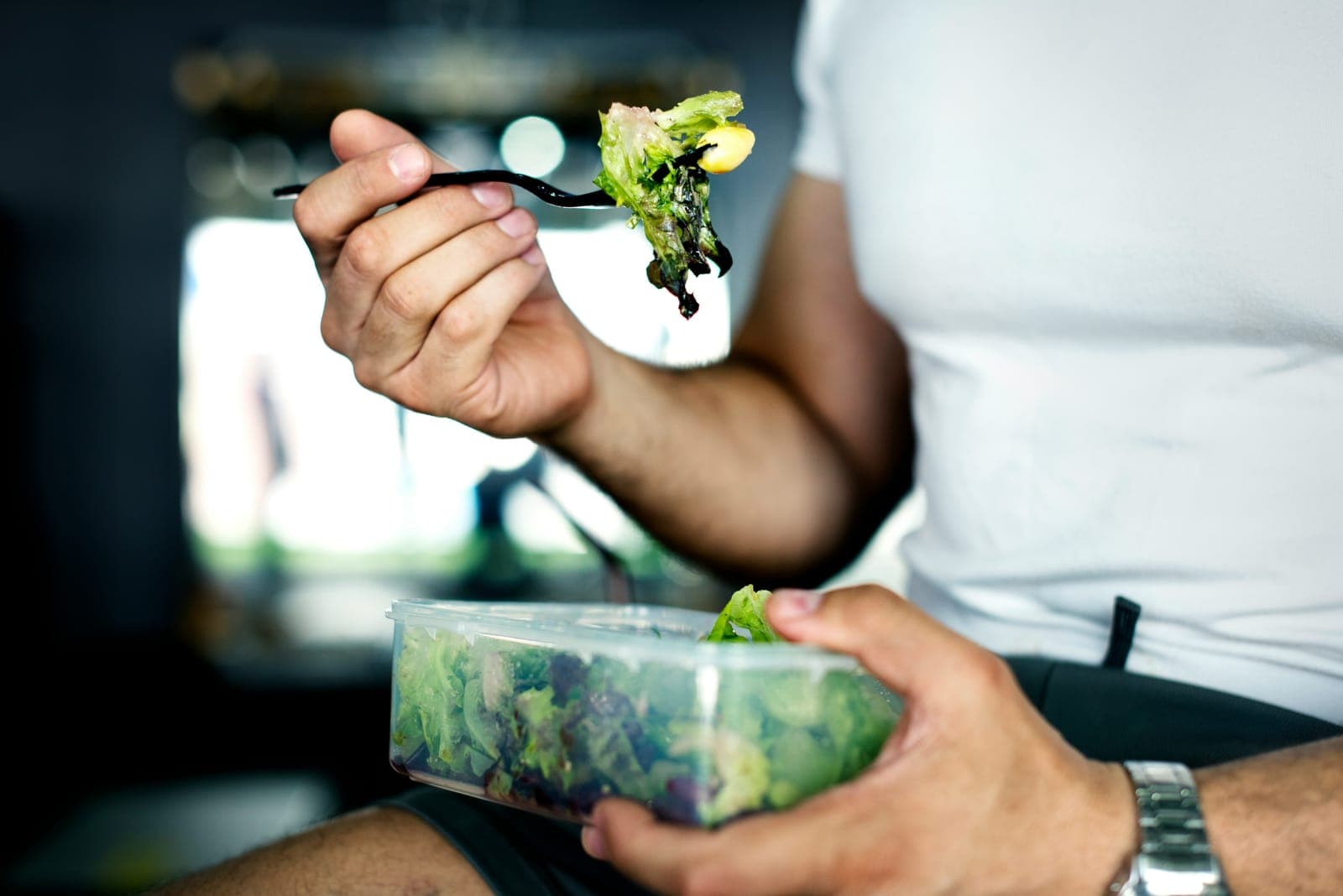 Person eating a fresh salad from a meal-prep container